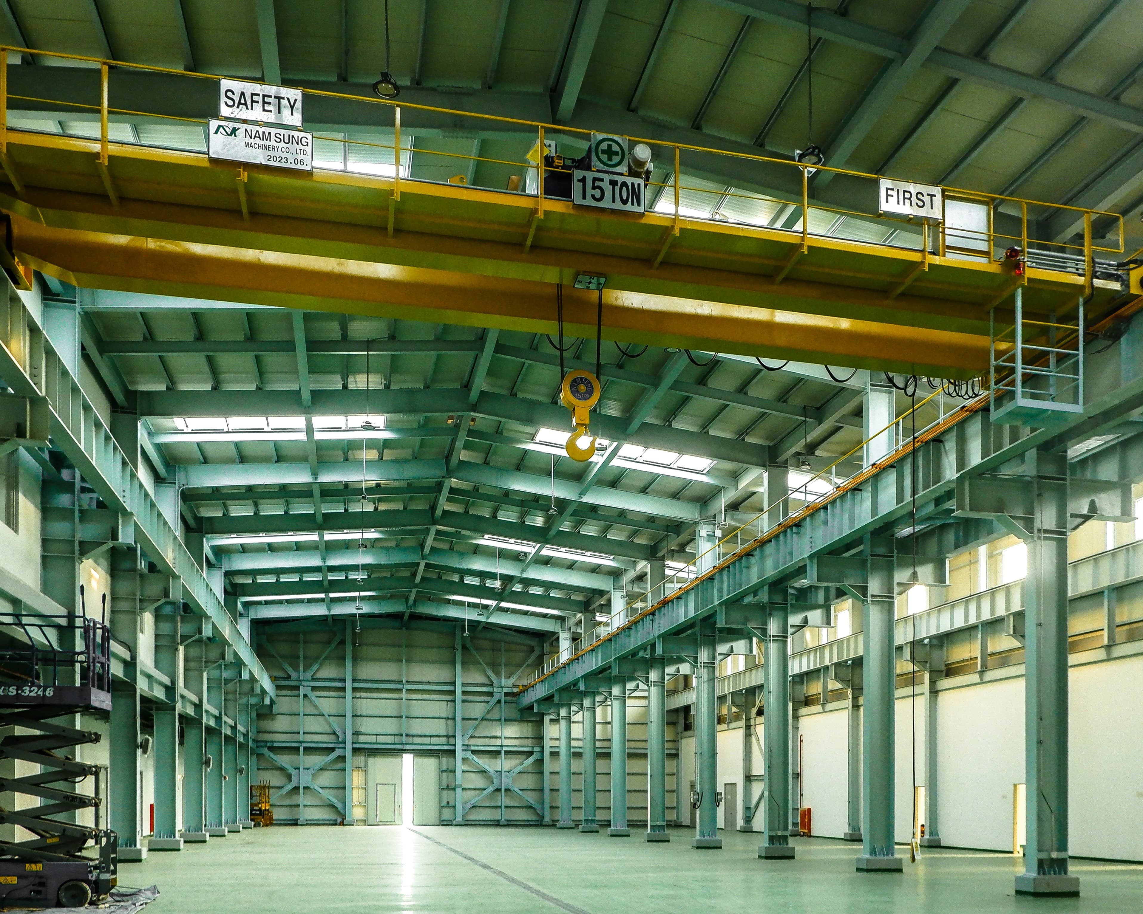 Interior of a modern industrial facility with teal structural steel, polished floors, and a yellow overhead gantry crane.